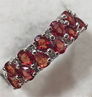 Close-up side angled view of silver ring with red-orange sapphires showing multiple stones set in prongs along the band.