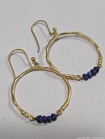 Pair of silver hoop earrings each with three dark blue lapis lazuli beads on the bottom, shown front view with ear hooks.