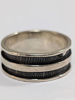 Close-up side view of silver ring showing two black textured bands between silver edges.