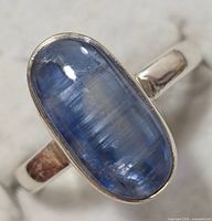 Top down close-up of ring showing large oval blue sapphire set in sterling silver band and bezel.