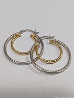 Pair of silver and gold-tone two-tone hoop earrings on white background