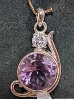 Close-up image of the silver amethyst pendant with diamond accent on dark background, showing the round faceted purple amethyst and clear gemstone above it in four-prong setting.