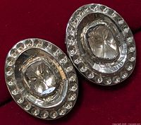 Pair of oval silver earrings with central marquise-shaped diamonds and surrounding smaller round diamonds on a red background.