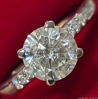 Close-up front view of round moissanite center stone with four prong silver setting and small accent stones on band.