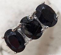 Close-up view of three oval dark blue sapphire stones set in sterling silver with prongs, showing facets and depth of stones