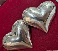 Pair of heart-shaped silver earrings on red fabric background showing reflective polished surface with minor wear marks.
