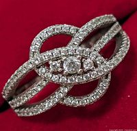 Close-up image of silver ring with an intertwined loop design studded with clear cubic zirconia stones, central larger stone visible.