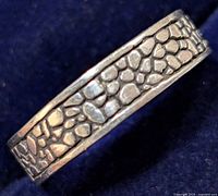 Close-up angled view of silver ring showing pebble pattern texture on the band.