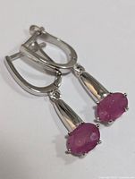 Front angle of the pair of silver earrings with oval ruby gemstones showing the polished finish and lever back fastening.