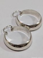 Pair of silver hoop earrings showing flat and smooth outside surface with latch backs closed.