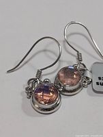 Clear close-up of two sterling silver earrings with round, faceted pink mystic topaz stones showing color and setting detail.