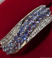 Close-up image showing the multi-row design of the silver ring with purple tanzanite and clear stones on a red background.