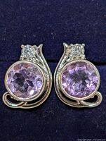 Close-up of the pair of silver earrings with round faceted amethyst stones and clear stone accents, showing front view and setting detail.