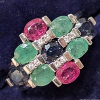 Close-up photo of the front view of the silver ring showing the ruby, sapphire, emerald and diamond stones set horizontally in three rows.