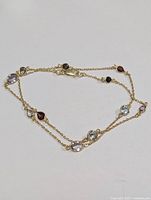 Sterling silver delicate chain necklace with assorted bezel-set multi-color gemstones laid flat to show chain and stones