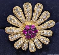 Close-up top view of the gold-tone silver floral ring showcasing the petals adorned with clear cubic zirconia stones and a center cluster of pink gemstones.