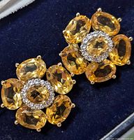 Close-up of one earring showing faceted citrine stones and halo of clear stones on silver setting against dark background
