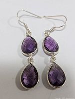 Front view of pair of silver earrings with two teardrop-shaped faceted amethyst stones each.