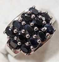 Close-up view of silver ring with 15 dark blue sapphire stones set in rectangular cluster pattern, showing prong settings and polished silver band.