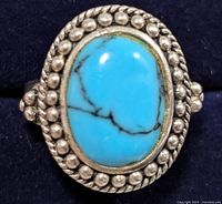 Close-up of the turquoise ring with silver beaded details on dark background.