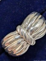 Close-up image of the sterling silver ring showing the ribbed broad bands tied at the center with a twisted knot design, capturing surface texture and shape.