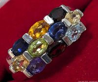 Close-up photo of silver multi-gemstone ring highlighting various colored oval gemstones set in silver band.