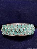 Top close-up photo of the silver ring featuring three rows of small round green emeralds set in prongs.