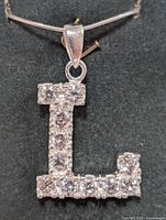 Front view of the silver necklace pendant shaped as the letter L, shows complete coverage with cubic zirconia stones.
