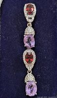 Front close-up of one earring showing garnet and amethyst gemstones with pavé accents