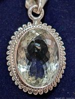 Close-up front view of oval faceted green amethyst pendant in silver setting on dark velvet background