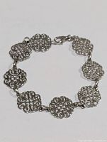 Full view of silver bracelet showing linked decorative filigree square components and lobster clasp