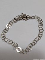Front view of the silver chain bracelet laid out in a curved circle, showing the detailed bead clasp and linked rings.