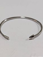 Side view of the silver bangle showing the pointed arrowhead end and smooth polished surface.