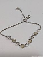 Close-up view of the silver adjustable bracelet laid flat, showing CZ stones and beige circular accents.