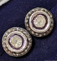 Close up front view of the pair of round silver earrings with central diamonds surrounded by smaller diamonds on dark velvety background.