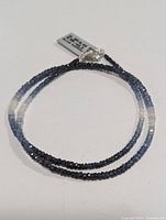 Full view of the silver and blue sapphire beaded necklace laid flat showing the color gradation of the beads and clasp.