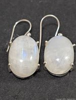 Pair of silver earrings with oval moonstone cabochons viewed from front against dark background.