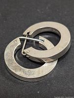 Pair of thick silver hoop earrings with hinged clasps photographed against a black background showing their size and condition.