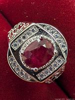 Close-up of silver ring showing oval ruby and cubic zirconia stones on red velvet background