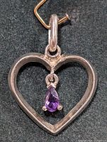 Close-up front view of a silver open heart pendant with a pear-shaped amethyst hanging inside.