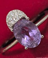 Close-up image of silver ring showing oval amethyst gemstone and half-moon shaped cubic zirconia cluster on a red background.