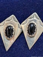 Close-up of one silver earring with black onyx stone, showing engraved triangular patterns and polished stone.