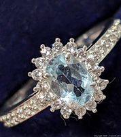 Close-up image of the ring top showing the oval faceted light blue blue topaz center stone with halo of small clear stones and clear stones on the band.