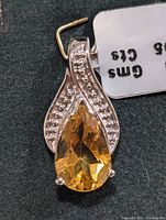 Close-up of silver pendant with pear-shaped citrine and diamond accent rows, showing tag details.