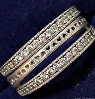 Close-up side angle of silver ring showcasing cubic zirconia rows and heart cutouts on central band.