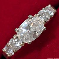 Close-up photo of silver CZ ring with oval central stone and smaller round stones on red background.