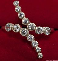 Close-up of silver ring with two crossing rows of round cubic zirconia stones against red background.