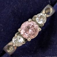 Close-up front view of the silver ring showing the round pink center CZ and two smaller clear CZ stones on each side set in prongs on a silver band with textured detailing.