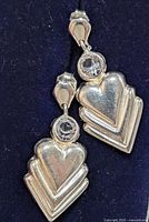 Pair of silver dangle earrings with clear round gemstones and layered heart shapes against a dark background.