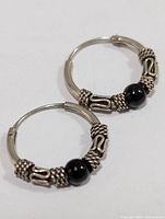 Close-up of one silver hoop earring with detailed coil and black bead embellishment.